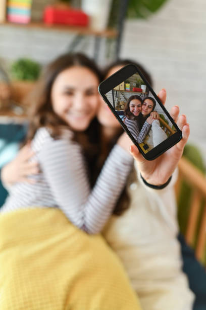 istock Good Looking Smiling Sisters Enjoying Cozy Sunday Evening Taking Selfie on Mobile Device 2176702010