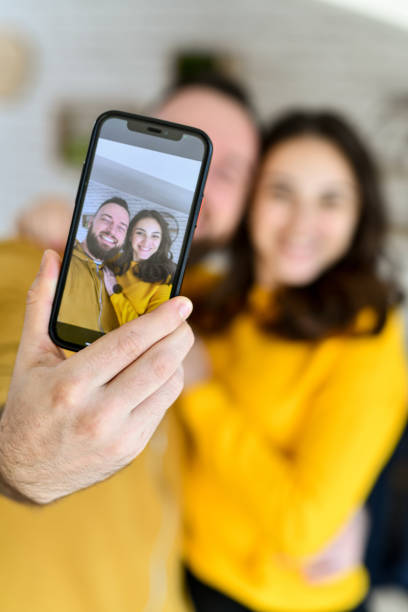 istock Young Good Looking Couple Taking Selfie on Mobile Device Before Going Out in Yellow Matching Outfits 2176702144