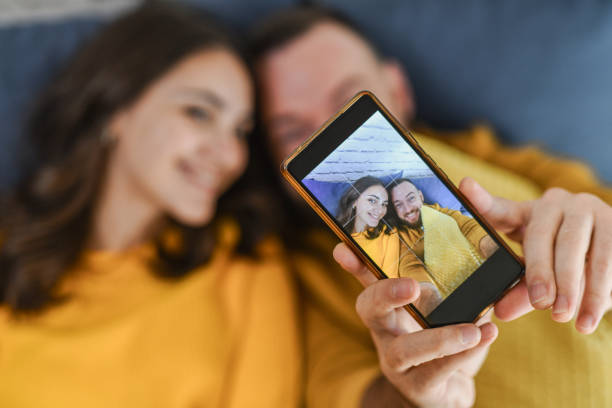 istock Beautiful Young Couple in Matching Yellow Sweaters Taking a Selfie on Mobile Device While Lying 2176702233