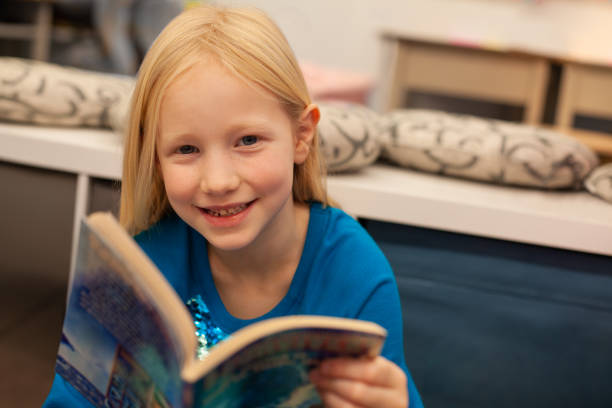 istock Portrait of girl elementary school student reading book in classroom library 2176704801