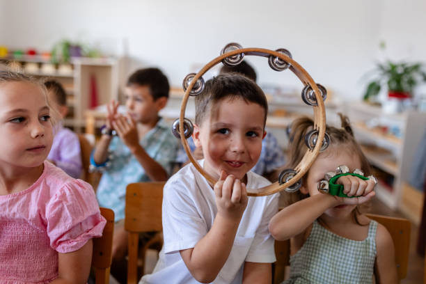 A child in a classroom confidently poses with a tambourine, part of an engaging music session where children learn to express creativity and develop musical skills.