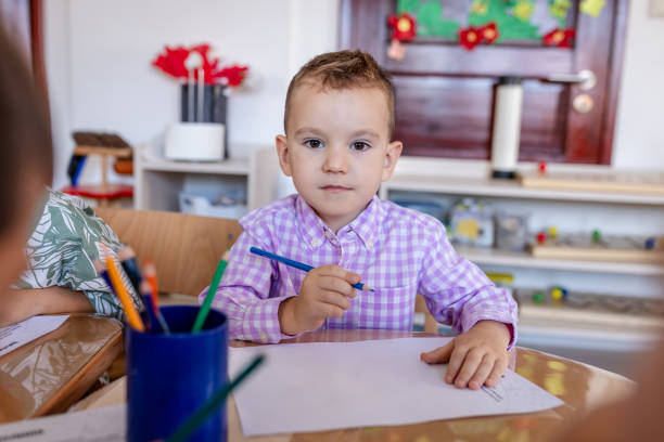 In a dynamic classroom setting, a boy in a checkered shirt is absorbed in his art project, surrounded by the bustling energy and creative spirit of his classmates.