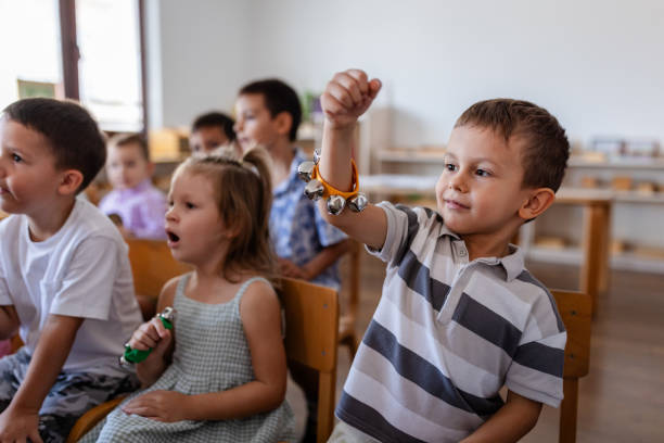 A young boy proudly holds up his tambourine during a classroom music session, where children explore sounds and rhythms as part of their educational experience.