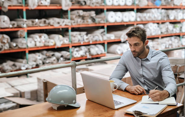 istock Warehouse manager checking stock with a laptop and writing notes 2176719338