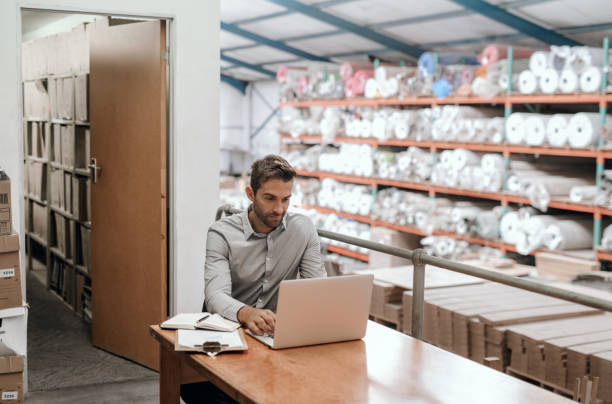 istock Smiling manager sitting in his warehouse office using a laptop 2176721276