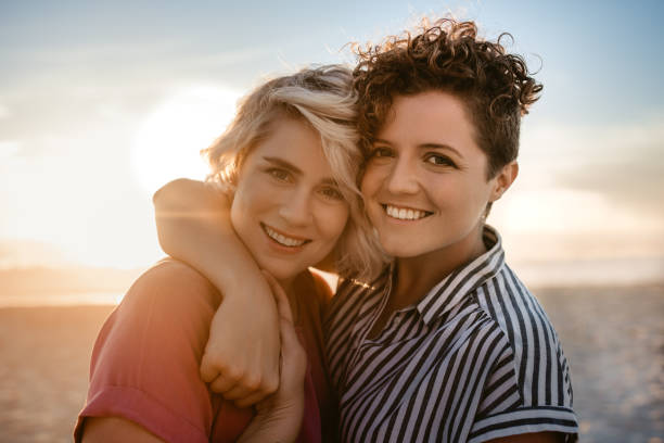 istock Smiling lesbian couple standing together on a beach at sunset 2176723835