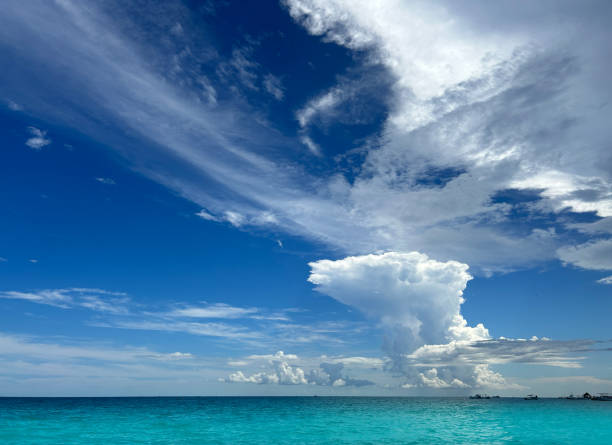 The scene features the stunning Caribbean Sea with its turquoise waters, complemented by a dramatic blue sky filled with fluffy clouds, typical of summer in Mexico's Mayan Riviera.