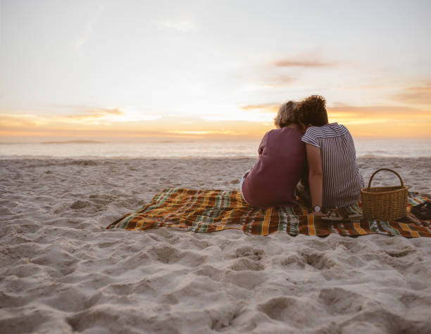 istock Young lesbian couple sitting on beach blanket watching the sunset 2176723996