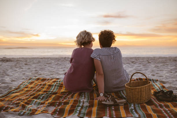 istock Young lesbian couple watching a romantic sunset at the beach 2176725032