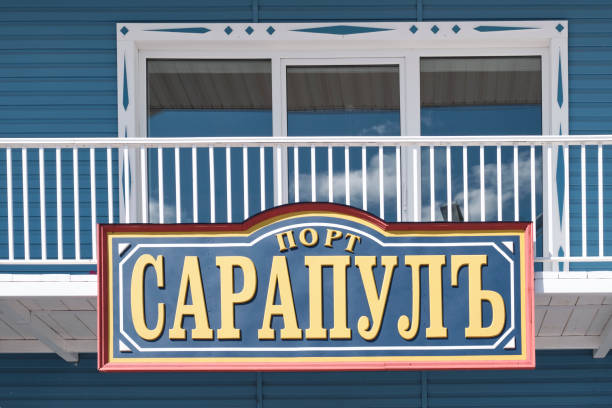 Sarapul, Russia - May 23, 2024: Text Port Sarapul. Sign with Old Church Slavonic script displayed prominently against blue wooden wall and white railing and large windows reflecting clouds above .