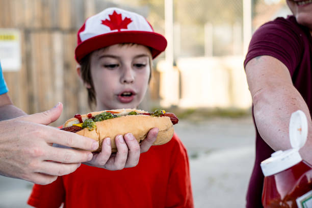 Hungry caucasian little girl looking at the camera holding a plate of hotdogs on gray background