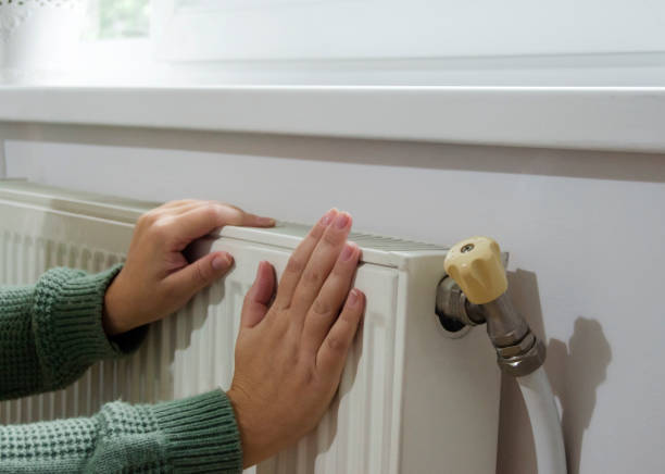 istock Woman's hand  touches heating radiator in home interior. 2176750505