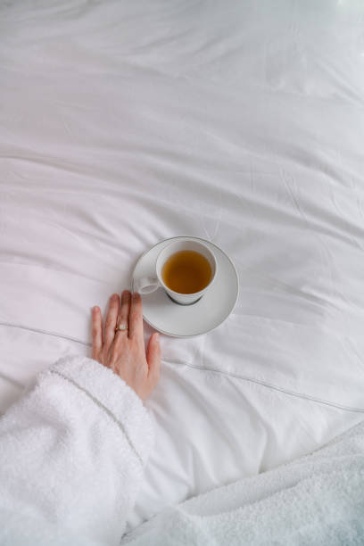 istock Woman wearing bathrobe relaxing in bed and drinking herbal tea 2176751395