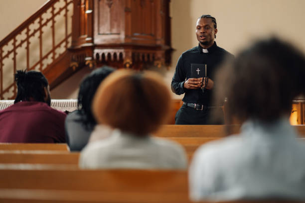 istock Young priest leading congregation in prayer holding bible 2176799577