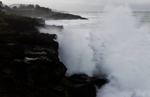 Large ocean waves crashing on rocky California pacific rocks, with clouds in the background.\n\nTaken at Pescadero State Beach, California, USA