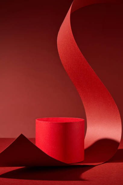 istock On a red backdrop, there is a lone red cylindrical podium. To create a dramatic image, a long strip of red paper is curled and stretched over the podium. A product presentation template picture. 2176831216
