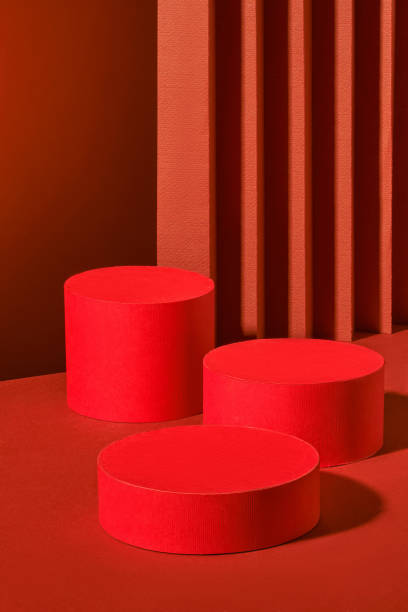 istock Three red cylindrical platforms, arranged in a minimalist manner against a backdrop of red vertical stripes, create a harmonious image. The platforms offer space to showcase various products. 2176831237