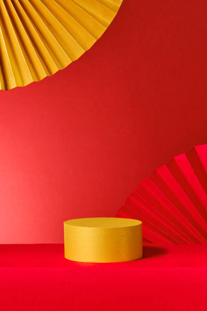 A visually striking product display featuring red and gold paper fans with a modern and abstract feel. A yellow cylinder sits prominently on a red base, serving as a platform for product showcasing.