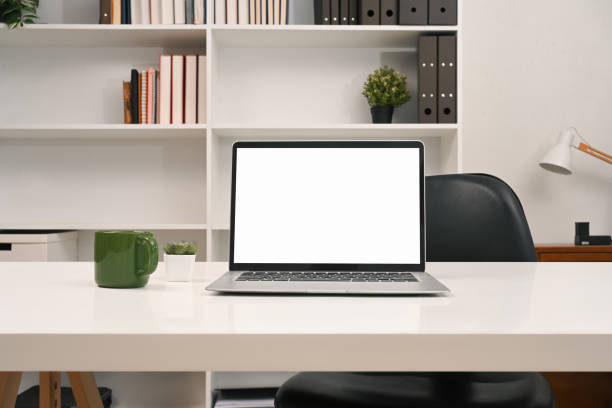 A laptop computer with empty display and office supplies on a desk in front of a bookshelf.