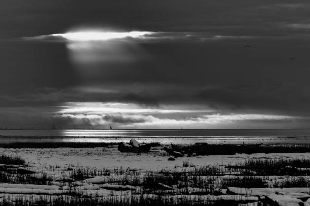 Black and white of a fisherman near the coast back-illuminated by the morning sun shining among the clouds