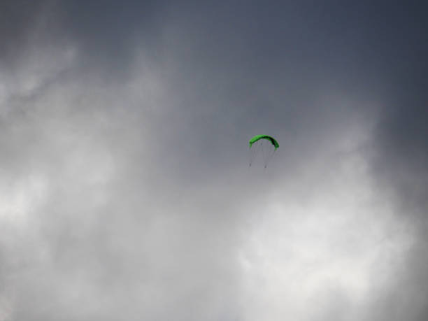 A small green kite is driven by strong wind and flying high in  the sky in front of dark and bright clouds