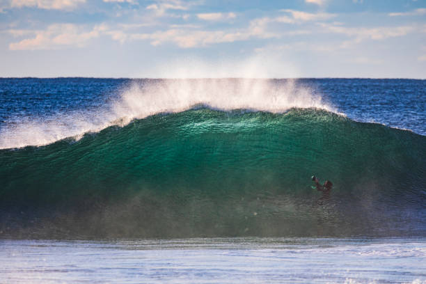 Camera man swimming under green wave forming in the ocean with dramatic golden light at sunrise. Photographed off the south coast of NSW, Australia.