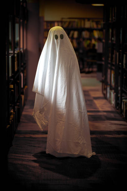 A child imitates a white ghost in a library room. Child dressed as a white ghost