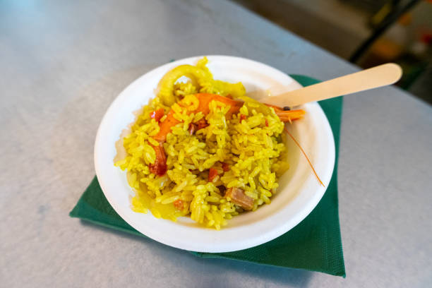 A vibrant seafood paella served on a disposable plate at a food festival, showcasing fresh ingredients and colorful presentation.