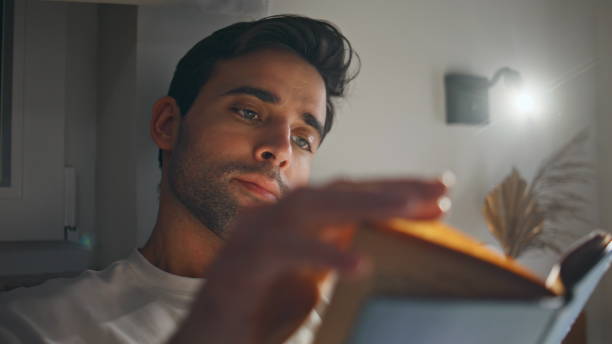 Guy engaged reading book under lamp light revealing focused demeanor closeup.