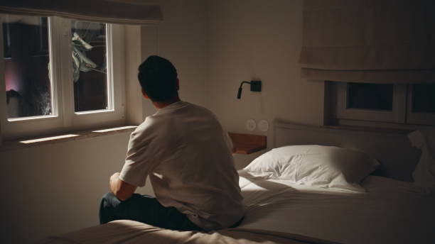 istock Sleepless guy holding mobile phone in dark bedroom. Tired man put down cellphone 2176897592