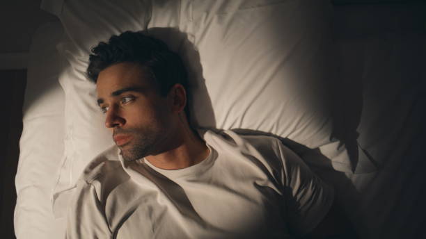 Man lying night bed suffering from insomnia closeup top view. Sad guy on pillow