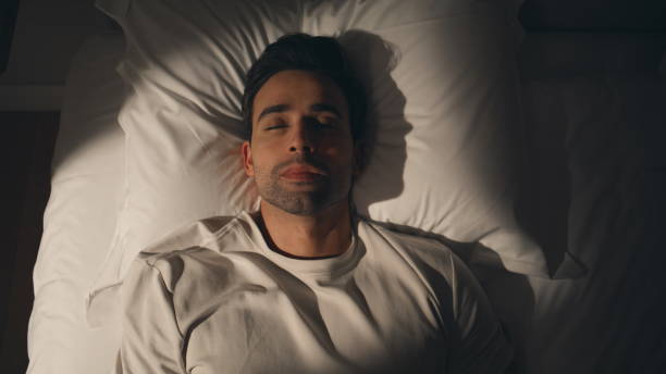 istock Guy lying dark bedroom at white bedding looking up closeup top view. Man on bed 2176900359