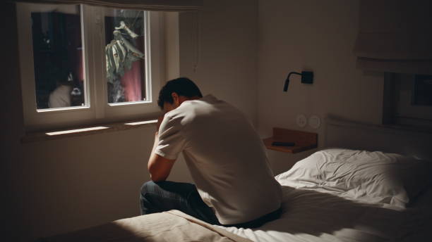istock Exhausted guy suffering insomnia at dark bedroom. Depressed man sitting home bed 2176900704