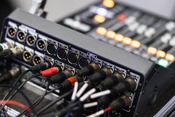 A musician in a warm recording studio holds a coiled cable while a connector is in focus, with drums and acoustic panels creating a creative audio engineering atmosphere.