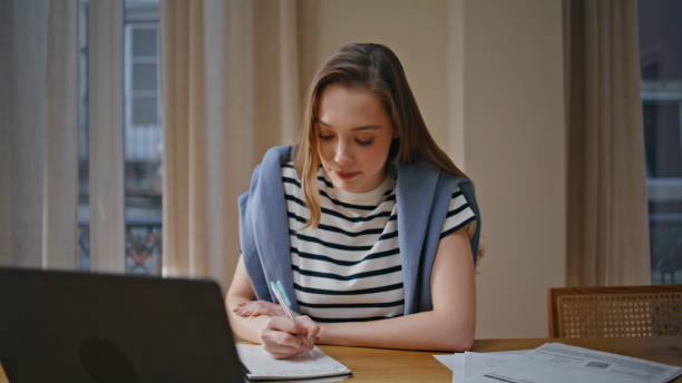 istock Woman teacher talking online lesson making notes in notebook at home closeup. 2176910310