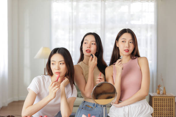 istock Three Young Women Applying Lipstick Together, Looking into a Mirror in Bright Room 2176918529