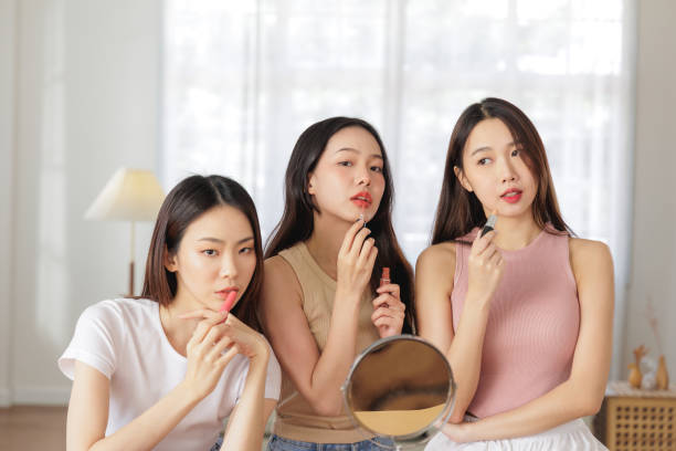 istock Three Young Women Applying Lipstick Together, Looking into a Mirror in Bright Room 2176918531
