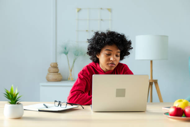 istock African american girl using laptop at home office looking at screen typing chatting reading writing email. Young woman having virtual meeting online chat video call conference Work learning from home 2176926865
