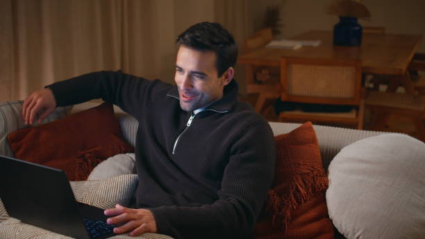 istock Joyful guy calling laptop on comfortable sofa at evening. Cheerful man talking 2176932849