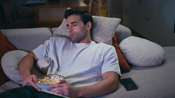 istock Closeup guy napping apartment sofa holding popcorn in tranquil home environment. 2176932977