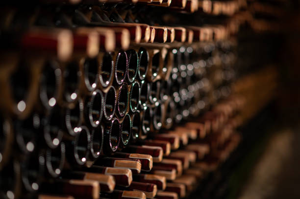 Row of wine bottles on a wooden shelf in a wine cellar stock photo