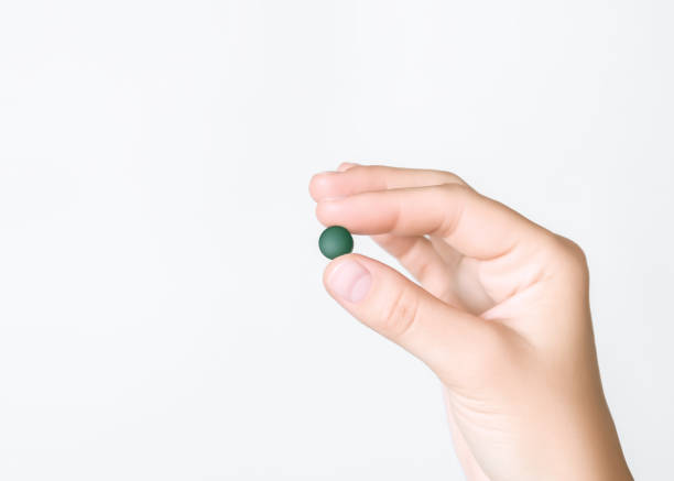 istock hand holding green chlorella and spirulina pill on grey background 2176935720