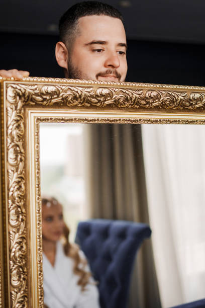 istock A man holds a large mirror in which a woman in a white coat reflects. 2176936998