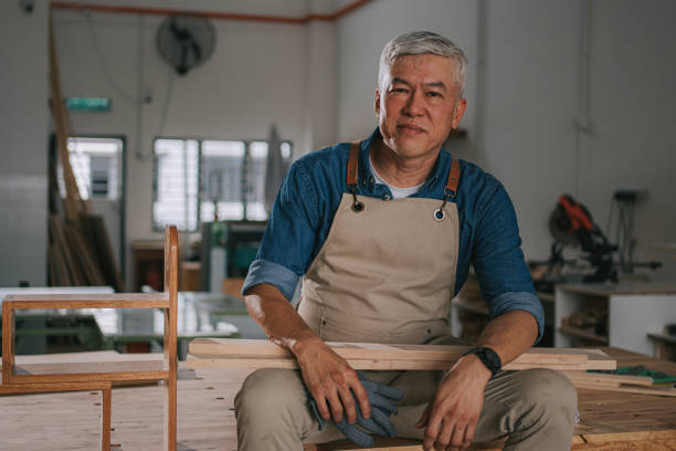 istock portrait successful asian senior carpenter looking at camera smiling sitting on workbench in workshop 2176939895