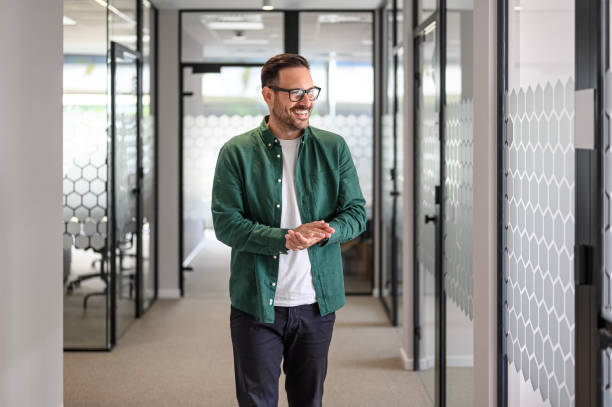 istock Handsome entrepreneur in glasses and with hands clasped looking away while walking in office corridor 2176944069