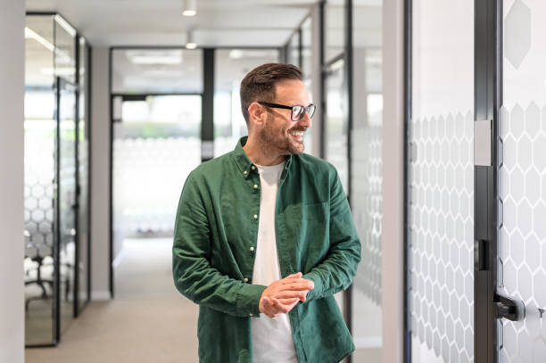 istock Happy male professional in eyeglasses looking away thoughtfully while standing in office corridor 2176944071