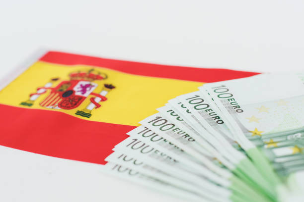 flag of spain and several 100 euro banknotes on white background.