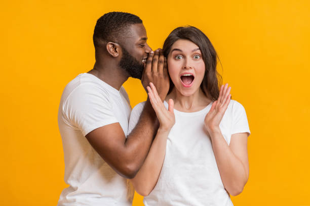 istock Smiling black guy whispering something into his shocked girlfriend's ear 2176953494