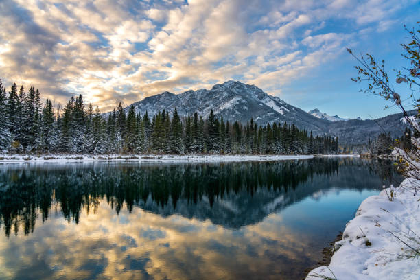Banff National Park beautiful natural scenery in winter sunset time. Mount Norquay with colourful clouds reflected on Bow River like a mirror. Town of Banff, Canadian Rockies.