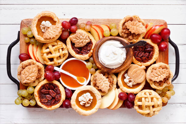 istock Fall pie theme dessert board. Overhead view table scene against a white wood background. Pumpkin, apple and pecan mini pies, with whipped cream, caramel and fruit. 2176959284